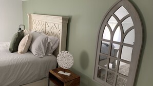 A bedroom with a bed, pillows, a bedside table, a decorative mirror, and a window with a view. - Cozy 3 bedroom 2 bath home close to hiking, biking, and Stowe! (Hyde Park)