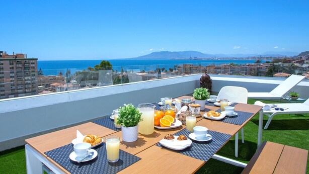 A balcony with a table set for breakfast, overlooking a coastal cityscape. - Genteel Home Elcano Terrace (Malaga)