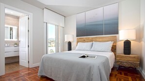 A bedroom with a large bed, two bedside tables with lamps, a view of the sea through a window, and a wooden floor. - Genteel Home Elcano Terrace (Malaga)