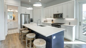 A modern kitchen with white cabinets, stainless steel appliances, and a large island with stools. - Dreamy beach escape on the 9th hole with balcony and WiFi - steps to pool (Port Aransas)