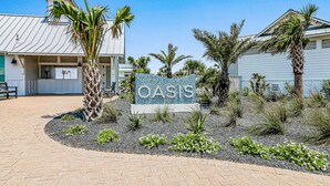 A sign for "OASIS" with a landscaped area featuring palm trees and shrubs. - Dreamy beach escape on the 9th hole with balcony and WiFi - steps to pool (Port Aransas)