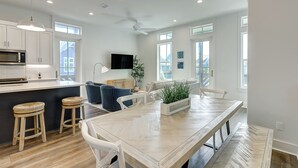 A modern kitchen with white cabinets, a built-in microwave, and a dining area with a wooden table and bar stools. - Dreamy beach escape on the 9th hole with balcony and WiFi - steps to pool (Port Aransas)