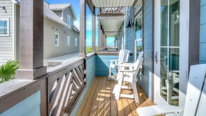 A wooden deck with white chairs, a glass door, and a view of neighboring houses. - Dreamy beach escape on the 9th hole with balcony and WiFi - steps to pool (Port Aransas)