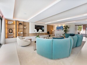 A modern living room with a large sofa set, a flat-screen TV, and a bookshelf.