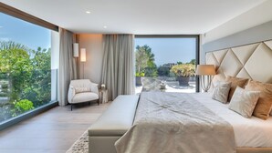 Une chambre moderne dotée d’un grand lit, d’un coin salon et offrant une vue sur la verdure et les bâtiments.