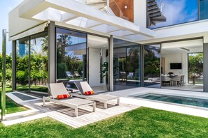 A modern house with a glass-enclosed patio, a pool, and a dining area with outdoor furniture. - All About Villa Gladiolo (Marbella)