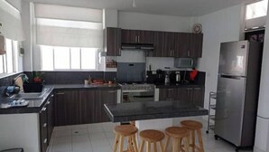 A modern kitchen with dark cabinets, a central island with stools, a stainless steel refrigerator, and a microwave.