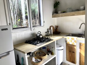 Eine kleine Küche mit Gasherd, Spüle und einem Fenster mit Blick auf einen Wald.