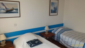 Una habitación de hotel con dos camas, una mesita de noche con lámpara y dos cuadros enmarcados en la pared.