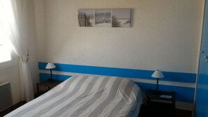 Una habitación con una cama, dos mesitas de noche con lámparas, un cuadro colgado en la pared y una puerta.