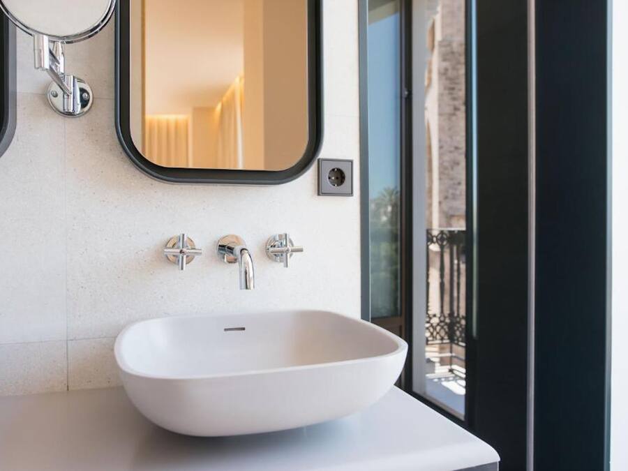 Un baño moderno con un lavamanos blanco, dos grifos cromados y un espejo encima.