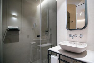 Un baño moderno con ducha envuelta en vidrio, un lavabo blanco y un espejo en la pared.