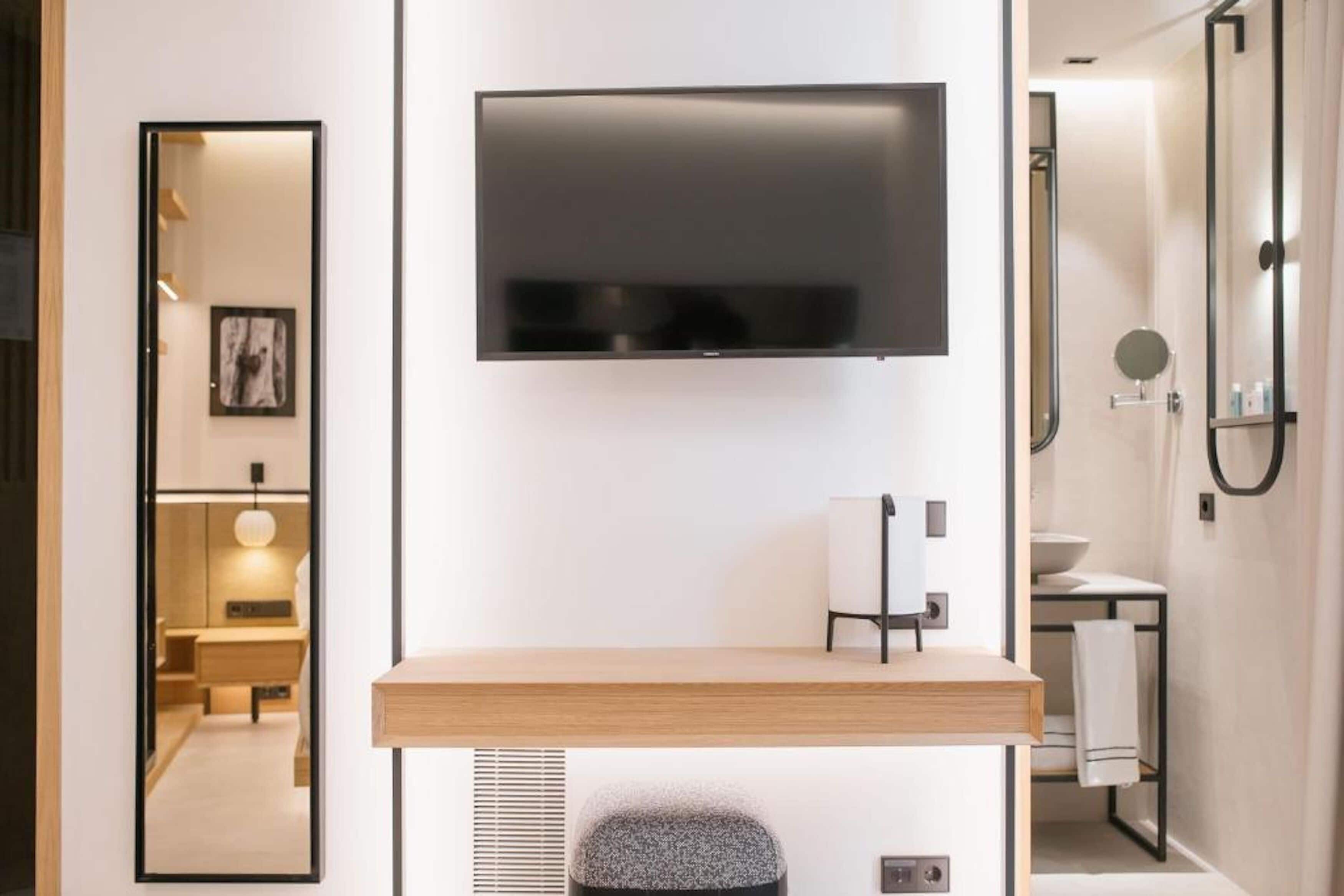 A modern bathroom with a mounted TV, a wooden vanity, and a shower area.