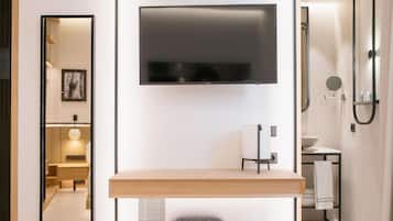 Un baño moderno con televisor montado, tocador de madera y zona de ducha.