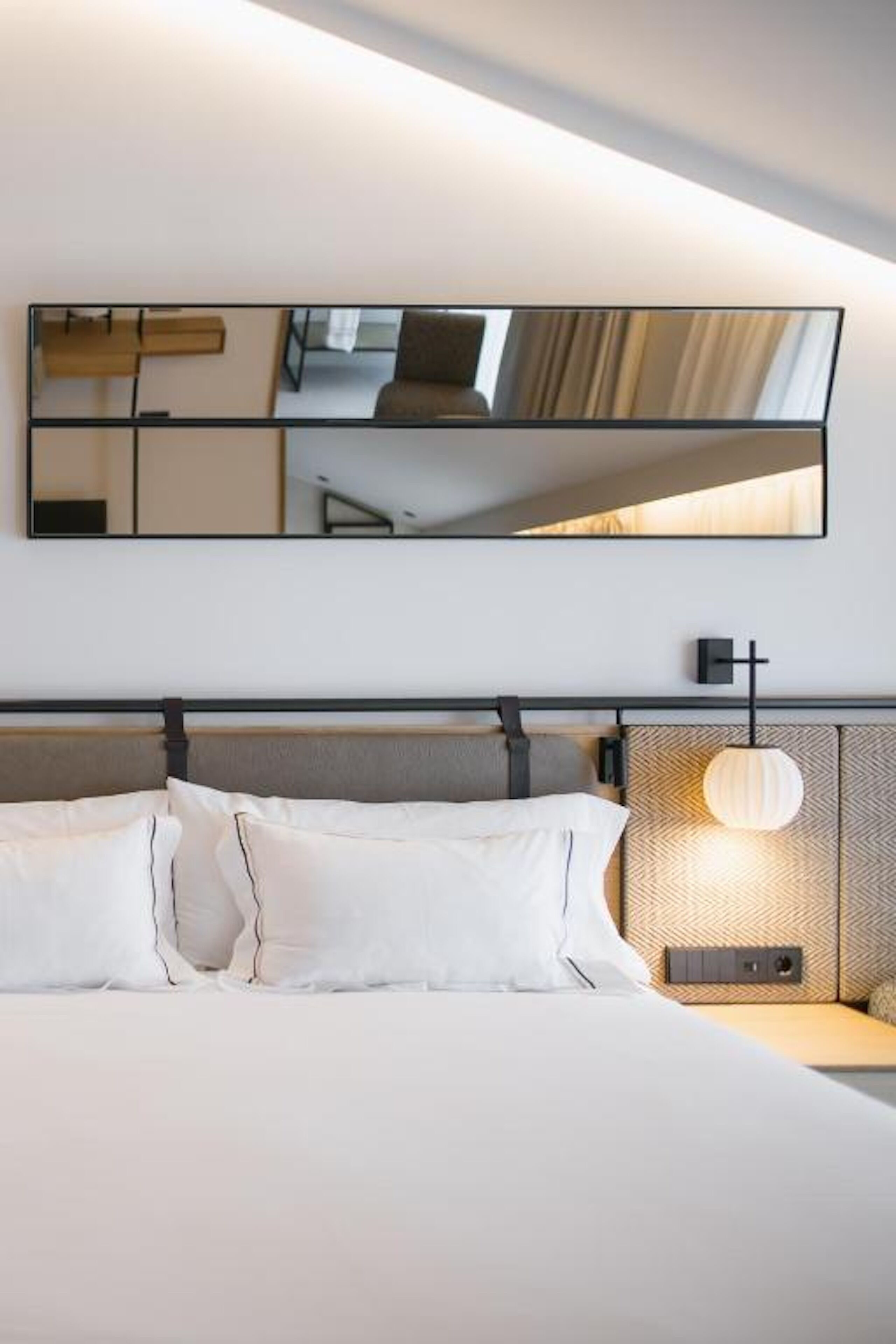 A modern hotel room with a large bed, a headboard with a built-in light, and a large mirror on the wall.