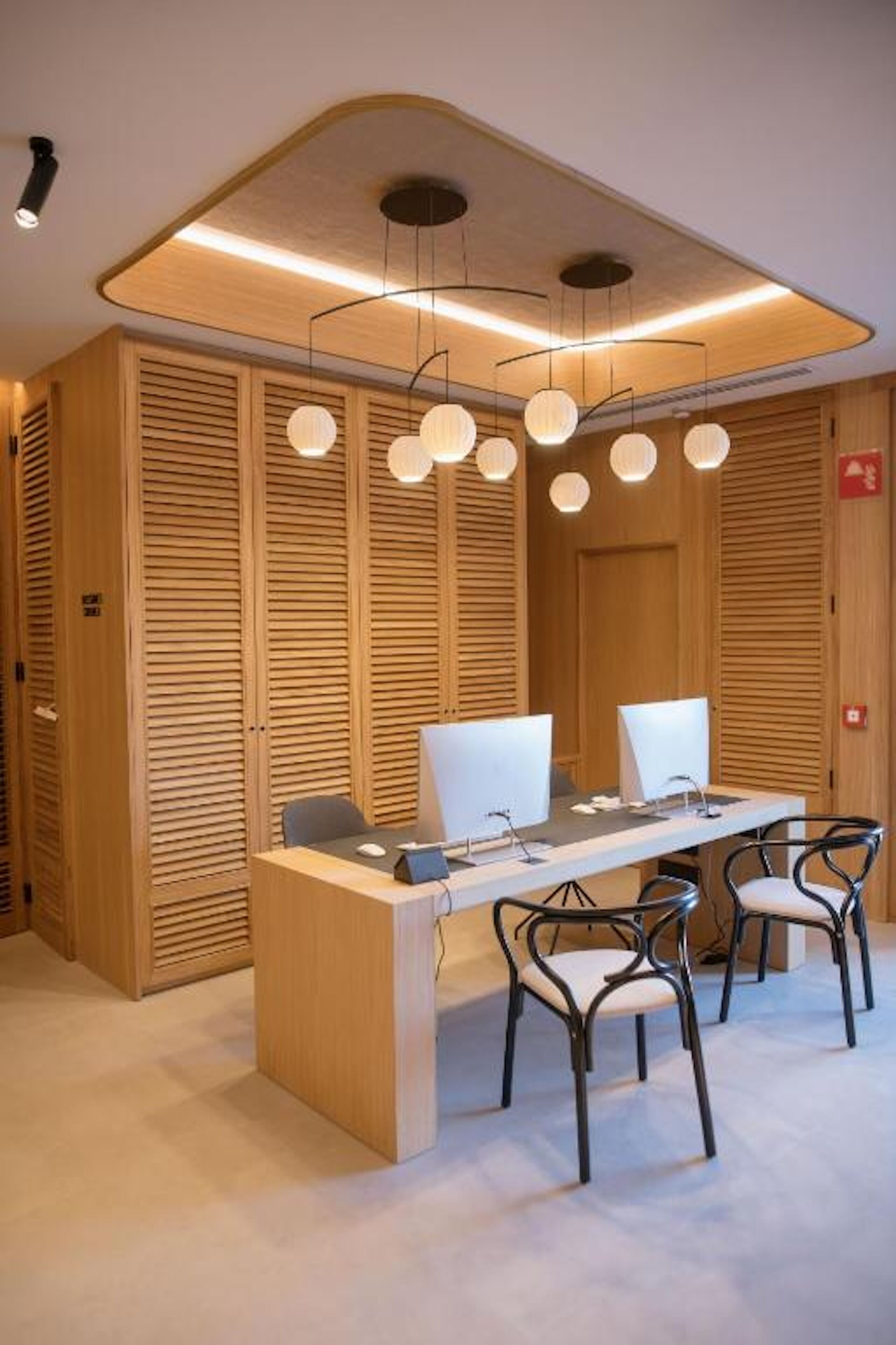 Une salle de conférence moderne avec un mur composé de lambris en bois, une longue table équipée de deux écrans et quatre chaises.