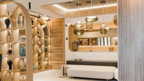A modern interior with a wooden shelving unit displaying various decorative items, a white bench, and pendant lighting. - MYR Puerta Serranos (Valencia)