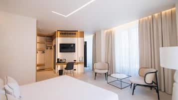 A hotel room with a large bed, a desk with a chair, a TV, and a seating area with two chairs.