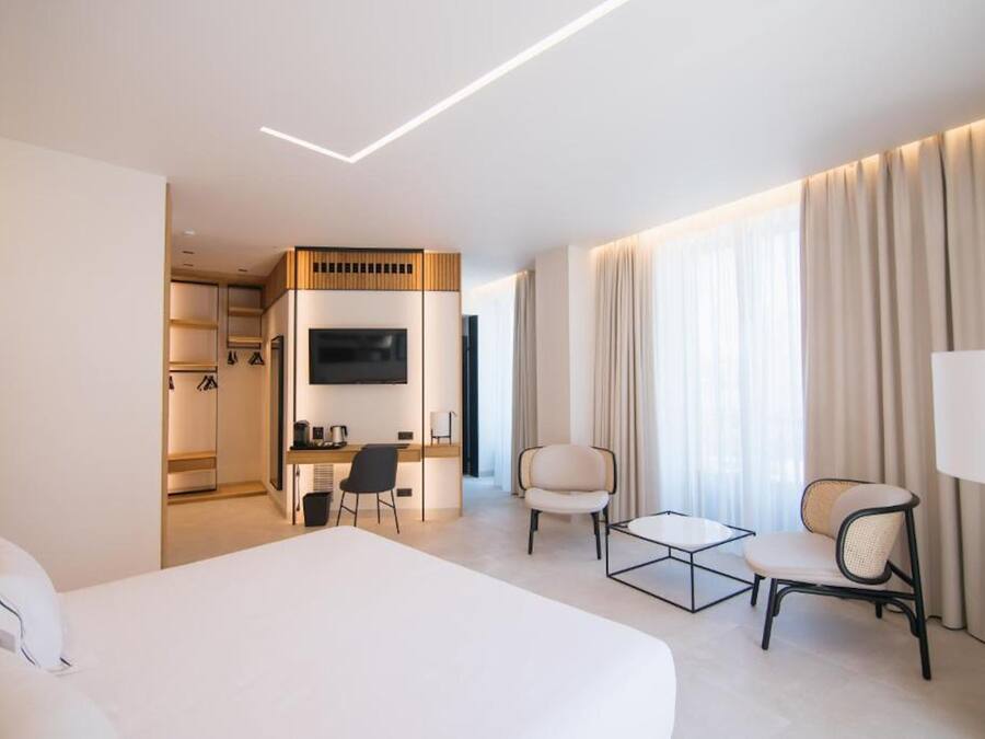 A hotel room with a large bed, a desk with a chair, a TV, and a seating area with two chairs.