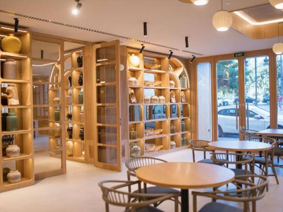 A modern interior with a round wooden table and chairs, surrounded by wooden shelving units with various items.