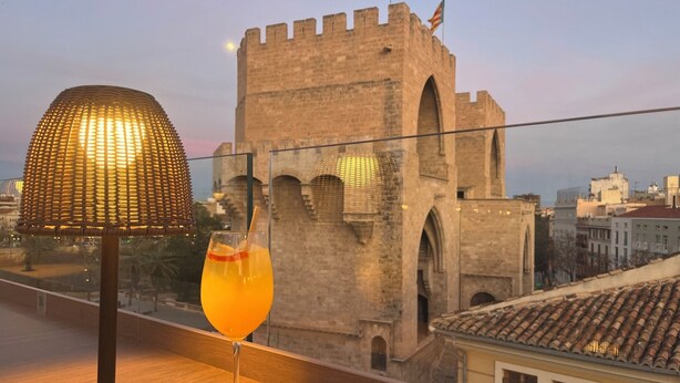 A balcony with a drink and a lamp, overlooking a historic building with arches and a flag. - MYR Puerta Serranos (Valencia)