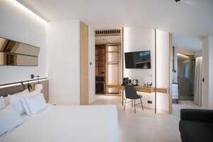 A modern hotel room with a large bed, a desk with a chair, a television, and a walk-in closet.