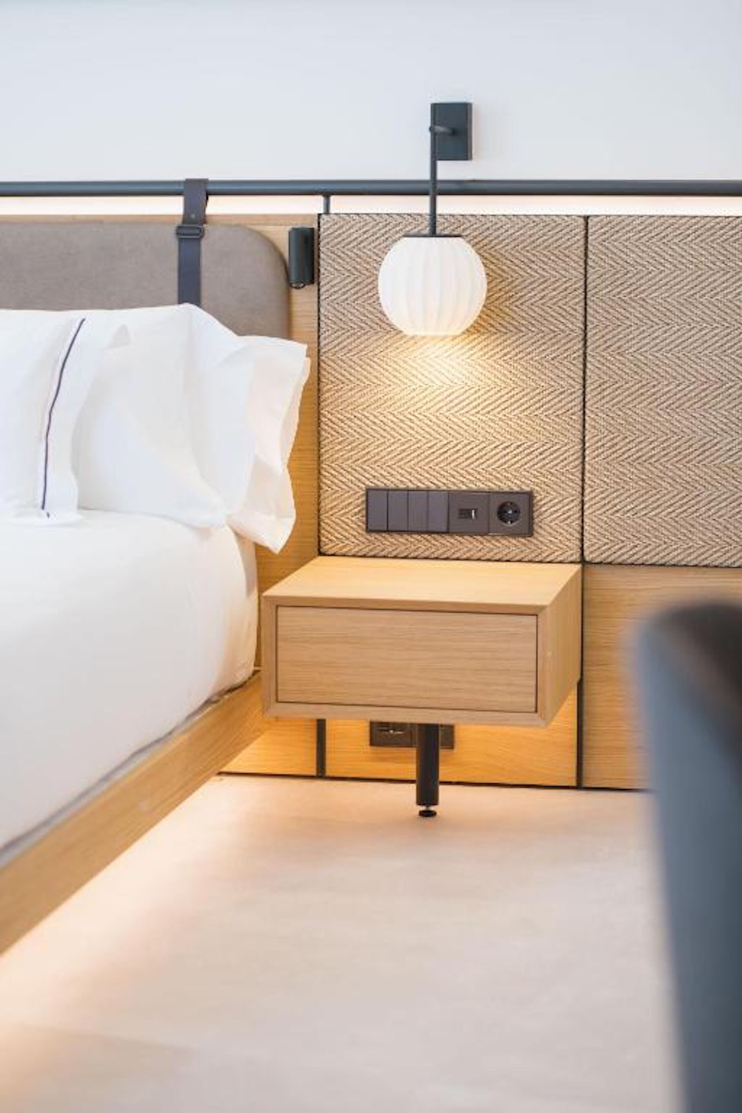A modern bedroom with a bed, bedside table, and a wall-mounted light fixture.