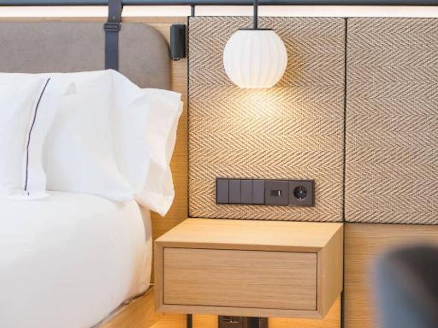 A modern bedroom with a bed, bedside table, and a wall-mounted light fixture.