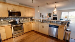 A modern kitchen with wooden cabinets, stainless steel appliances, and a dishwasher. - Calliope's Seaside Sanctuary Condominium - Oyhut Bay Seaside Village (Ocean Shores)