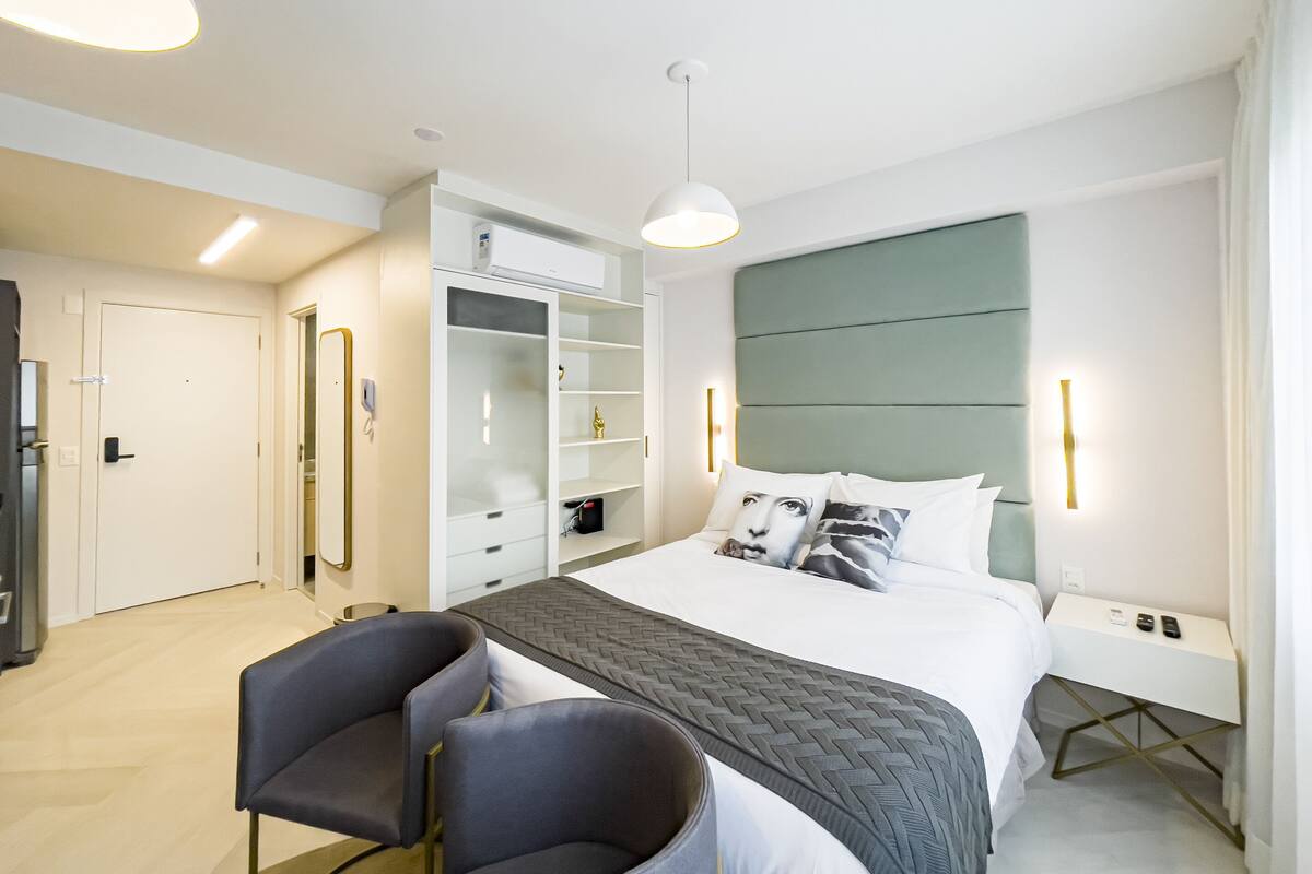 A modern hotel room with a bed, bedside tables, a wardrobe, and a seating area.