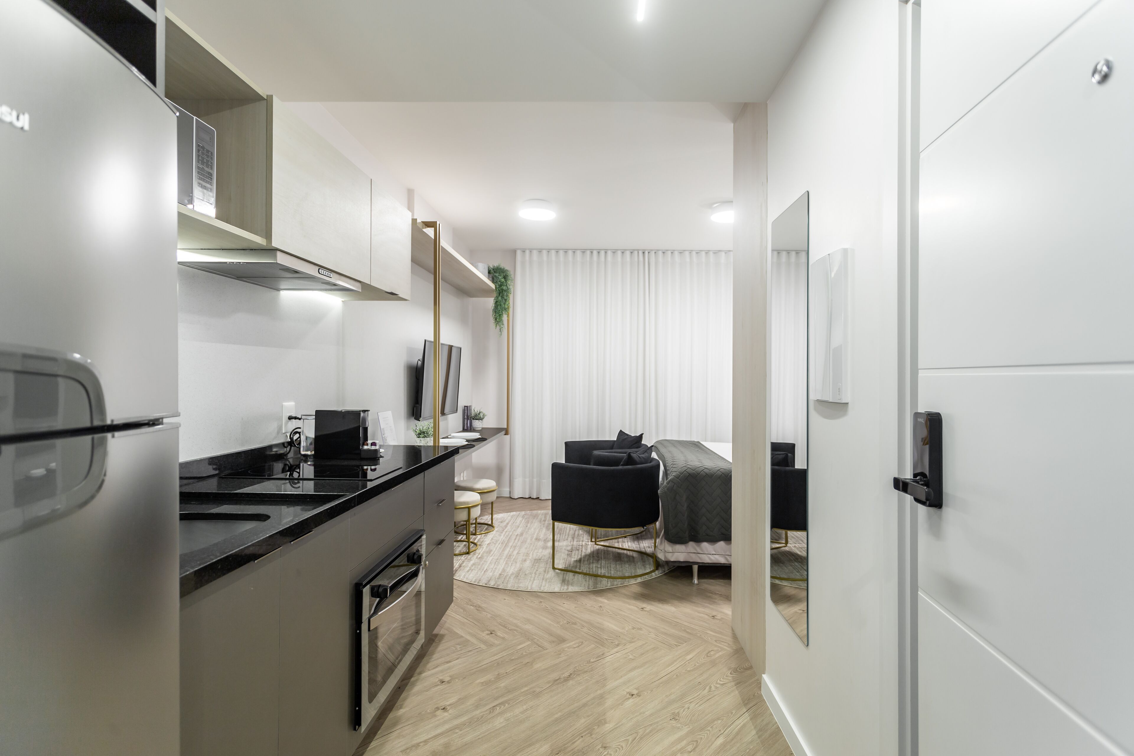 Una cocina moderna con refrigerador, estufa y microondas. Hay un comedor con mesa y sillas. Se ve una cama al fondo.