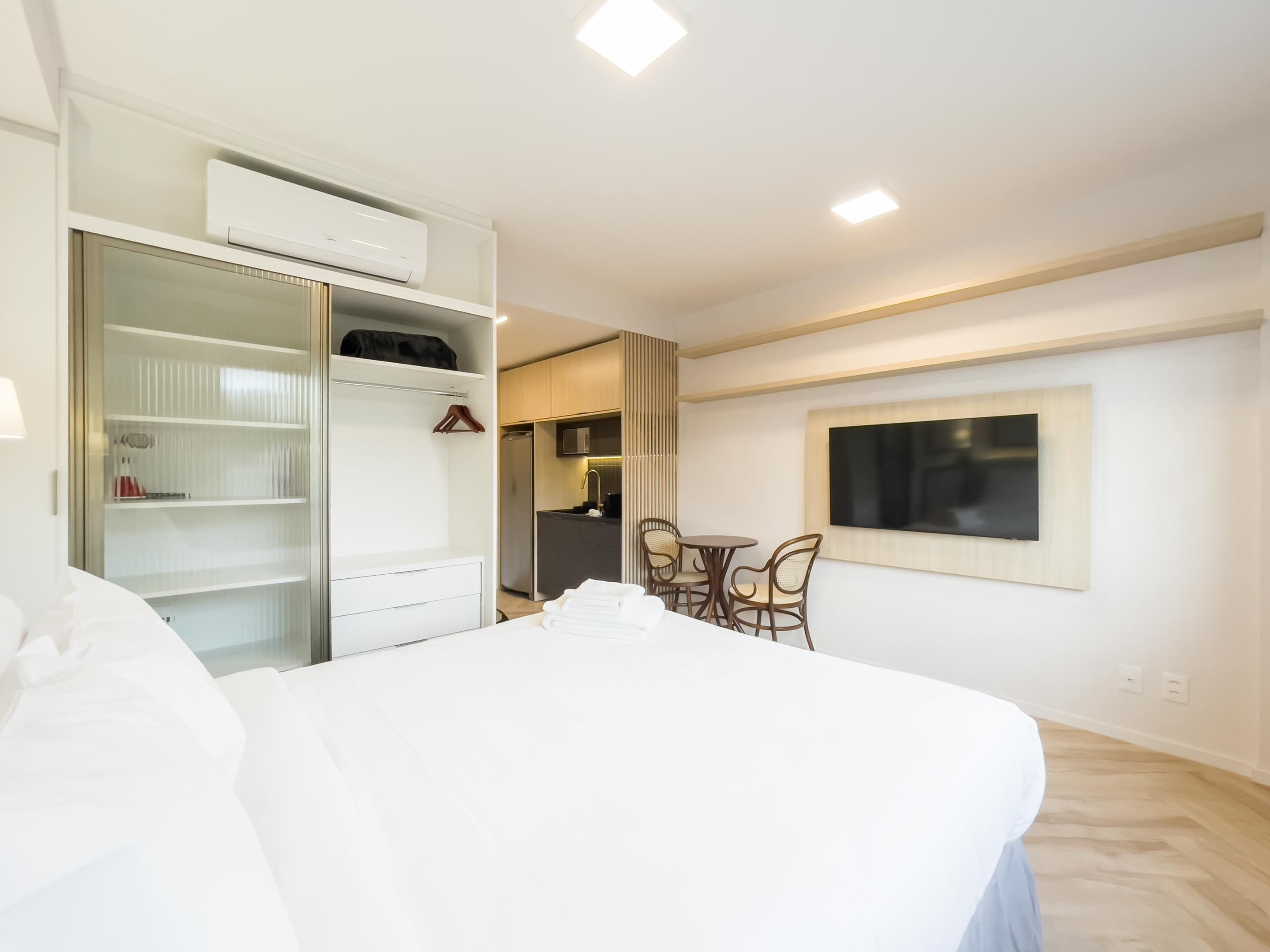 Hotelkamer met een bed, een kledingkast, een klein kitchenette, een eethoek met stoelen en een aan de muur bevestigde televisie.