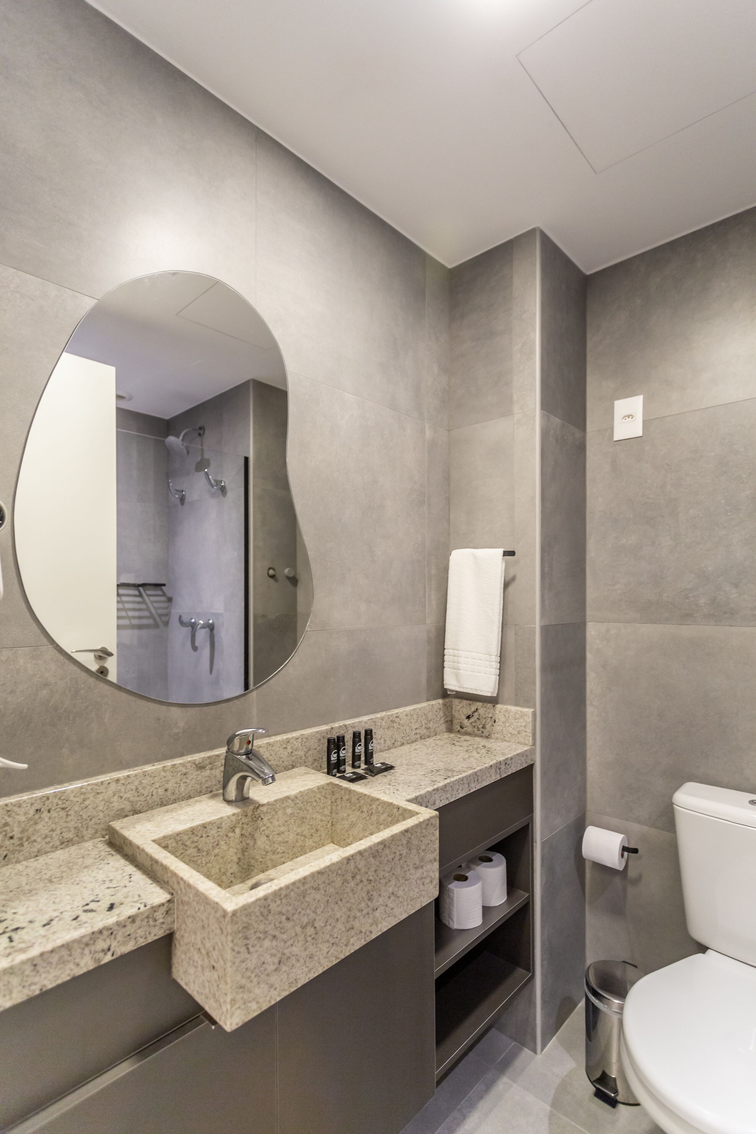 A modern bathroom with a granite sink, a large mirror, a toilet, and a shower area.