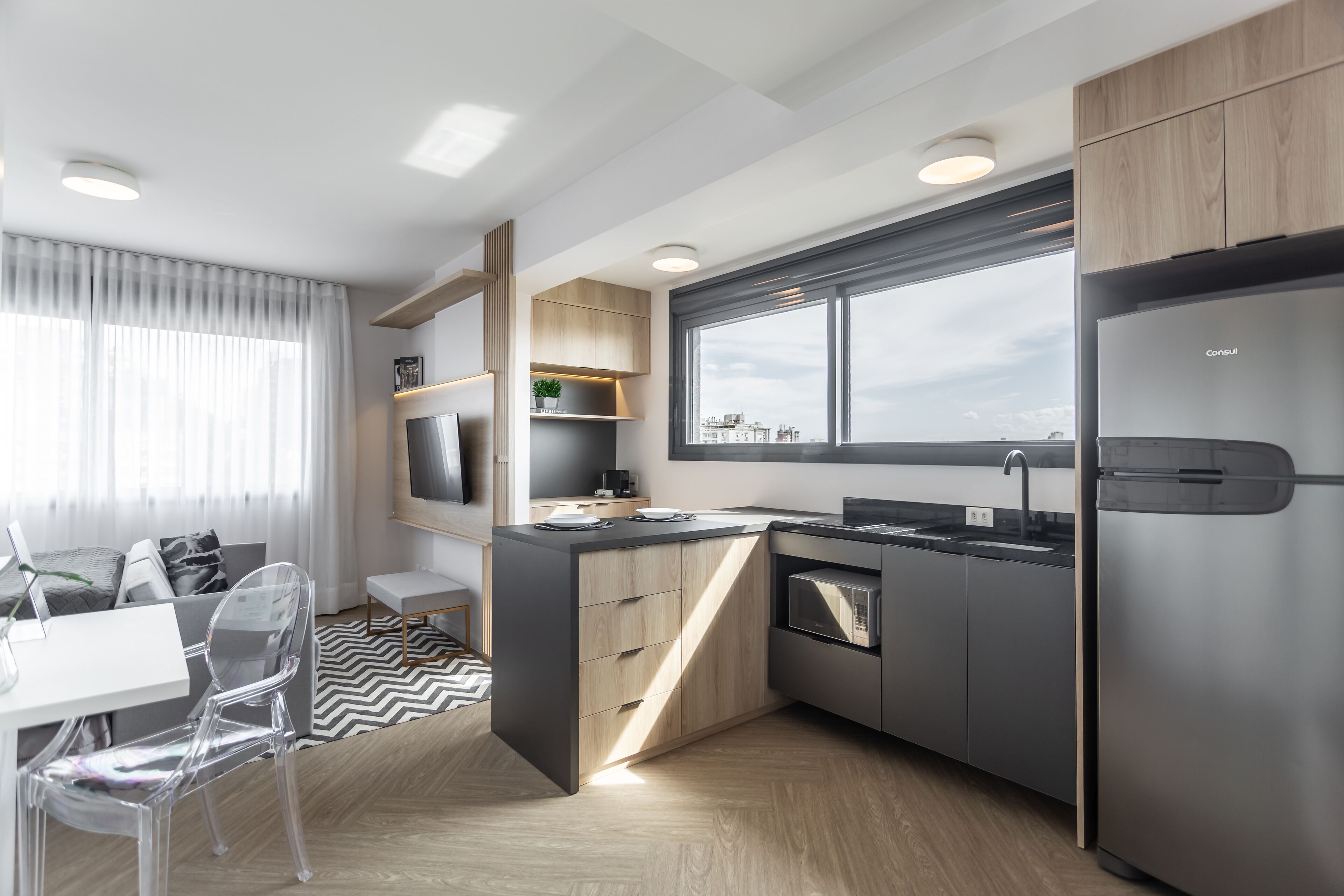 A modern kitchen with a built-in oven, a stainless steel refrigerator, and a window overlooking the city.