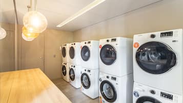 A row of Samsung washing machines in a laundry room with a wooden table and a hanging light fixture.