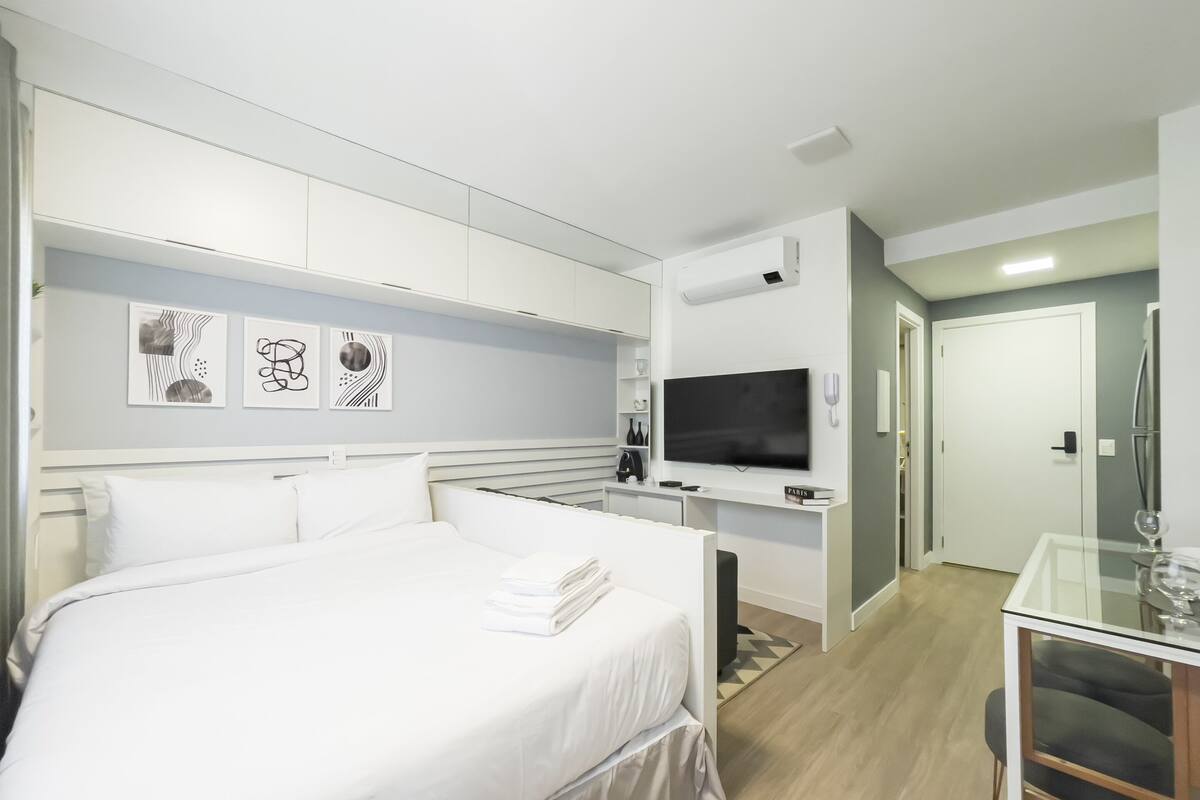 A modern hotel room with a large bed, a desk, a flat-screen TV, and a minibar.