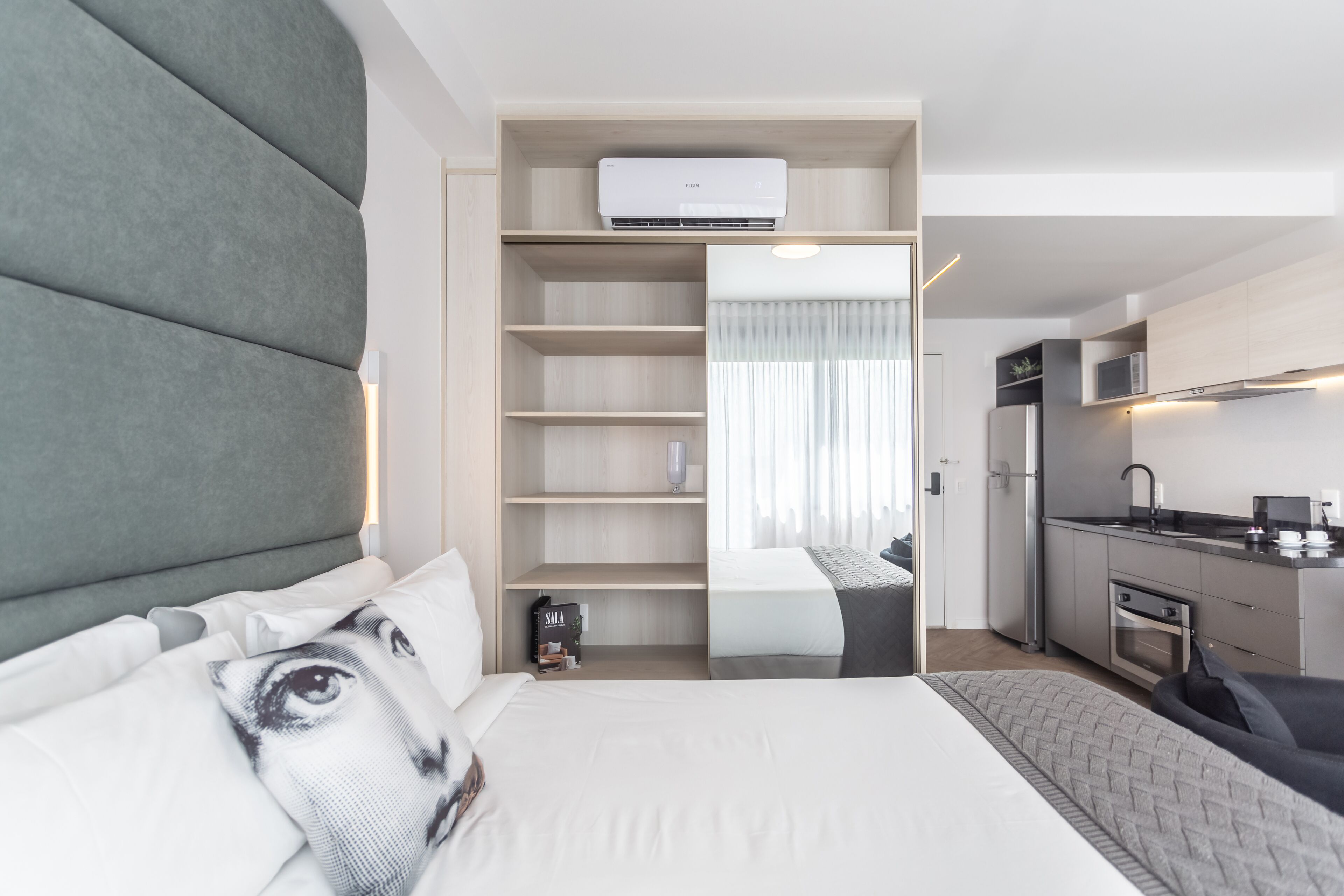Una habitación de hotel moderna con cama, armario empotrado, kitchenette y un ventanal grande.