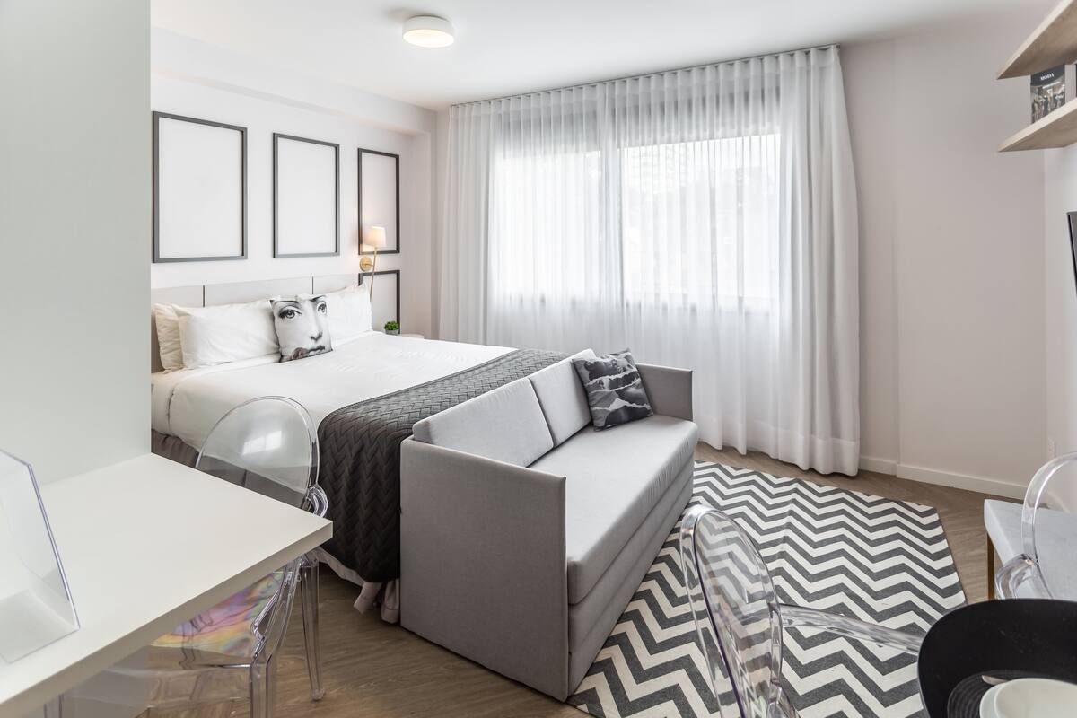 A modern hotel room with a bed, a sofa, a desk, and a chair.