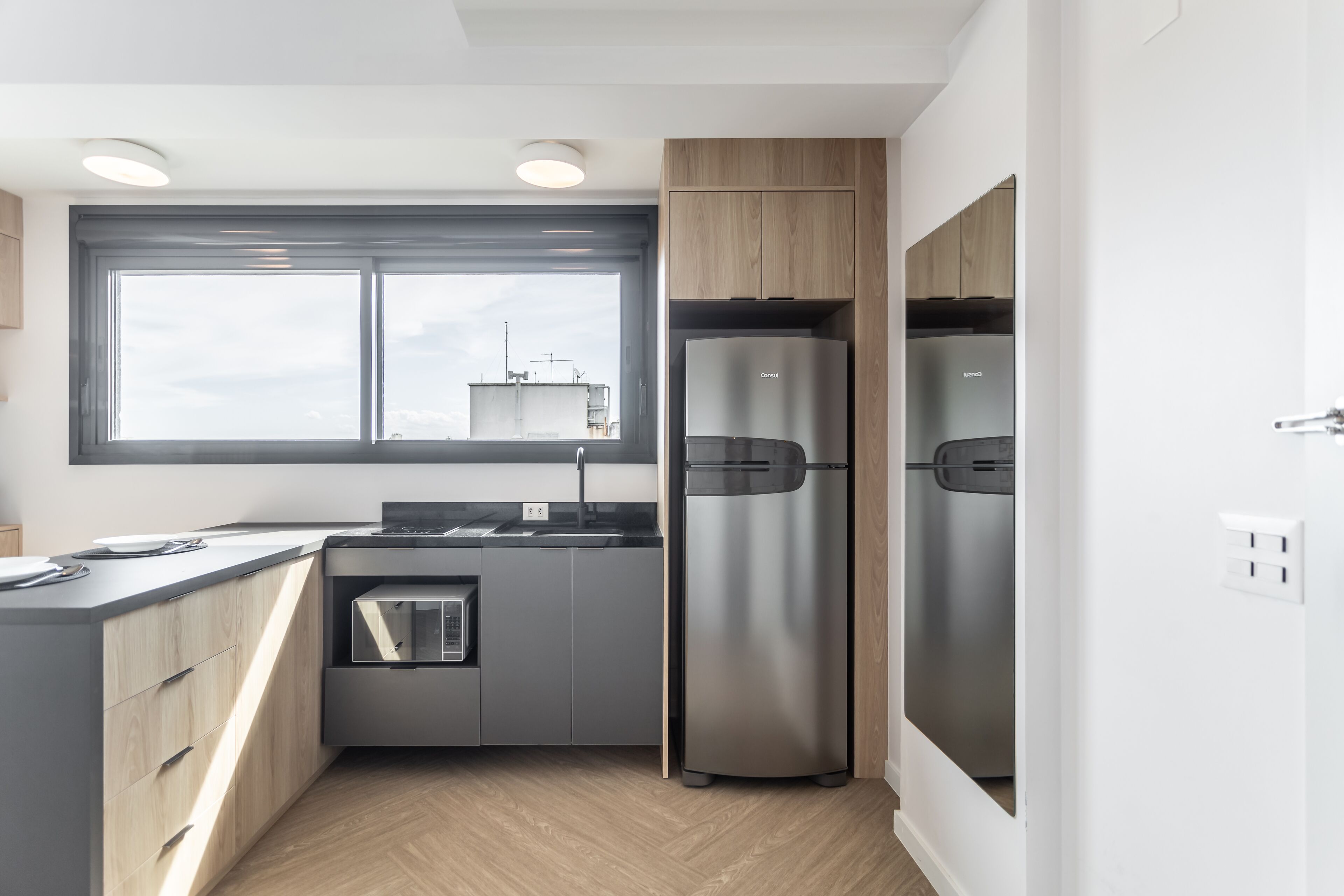 Una cocina moderna con refrigerador integrado, un lavamanos y un ventanal que proporciona luz natural.