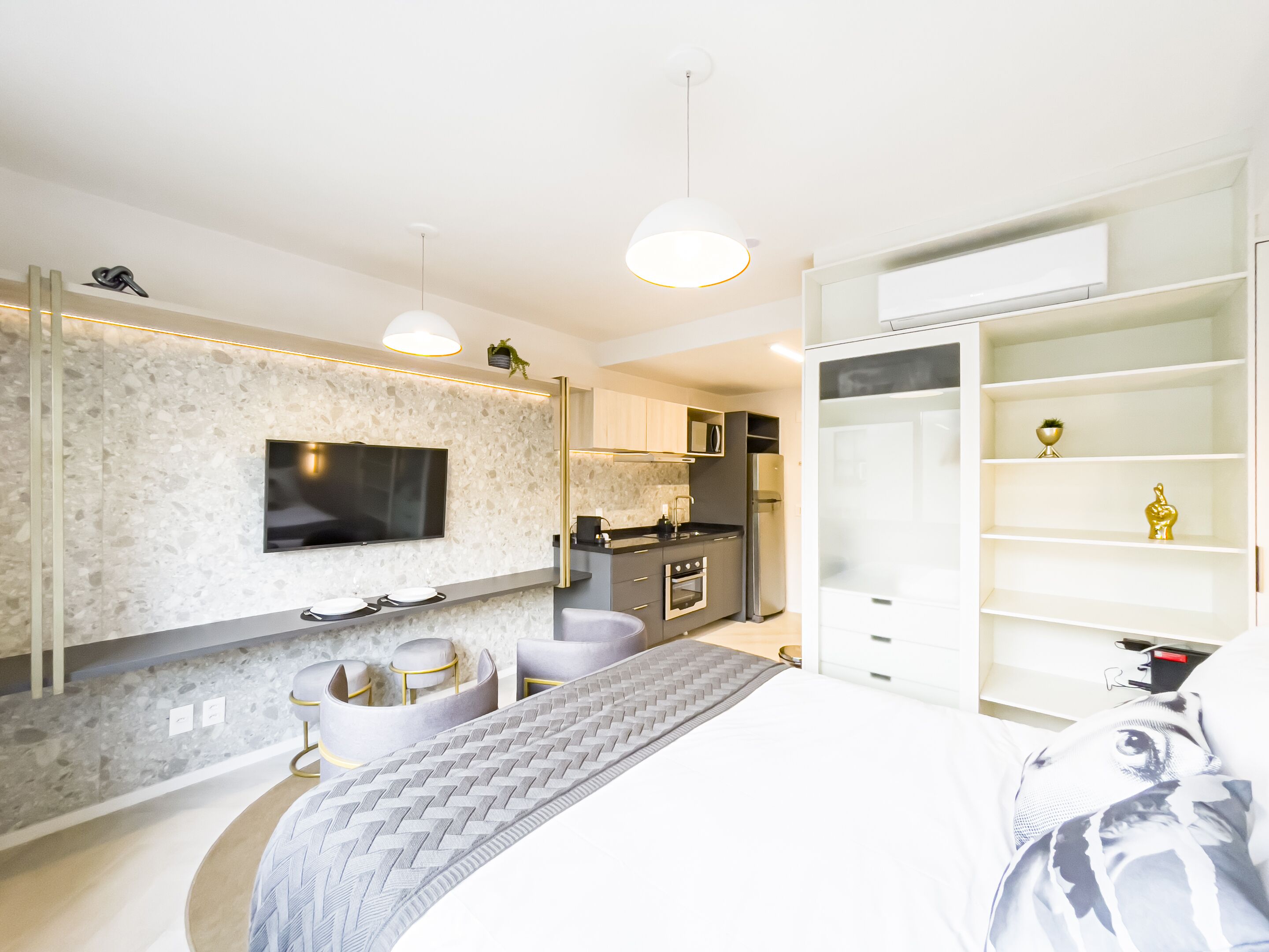 Un dormitorio moderno con una cama grande, un televisor instalado en la pared, una zona de cocina y un armario empotrado.