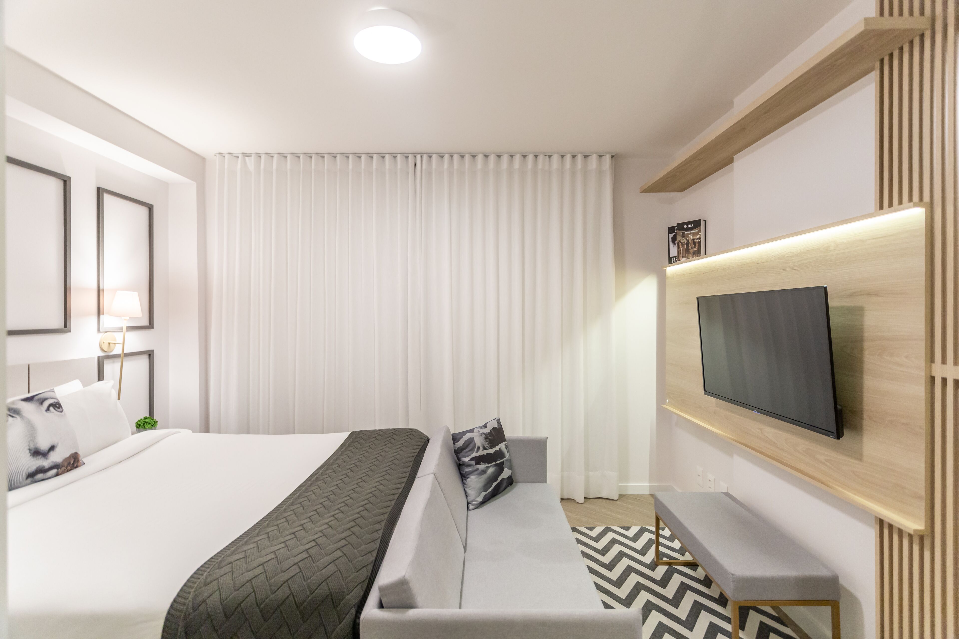 Ein modernes Hotelzimmer mit einem großen Bett, einer Couch, einem an der Wand befestigten Fernseher und einem Nachttisch.