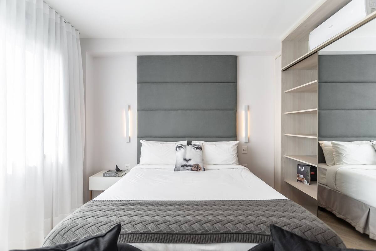 A modern hotel room with a large bed, a bedside table, a wardrobe, and a view of the city.