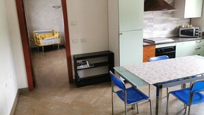 Une cuisine compacte équipée d’un four à micro-ondes, d’une cuisinière et de placards. Une table à manger avec des chaises se trouve au premier plan.