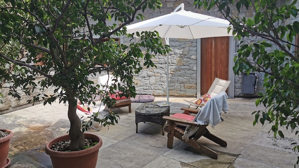 Un espace patio agrémenté d’un mur en pierre, d’une table en bois, d’une chaise et d’un grand parasol offrant de l’ombre.