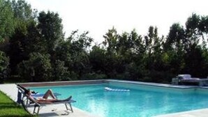 Une piscine rectangulaire avec un fauteuil de relaxation et une petite table sur la terrasse.