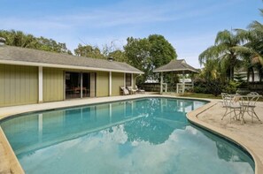 Una piscina con bordo curvo, circondata da un portico coperto con sedie e un tavolo.