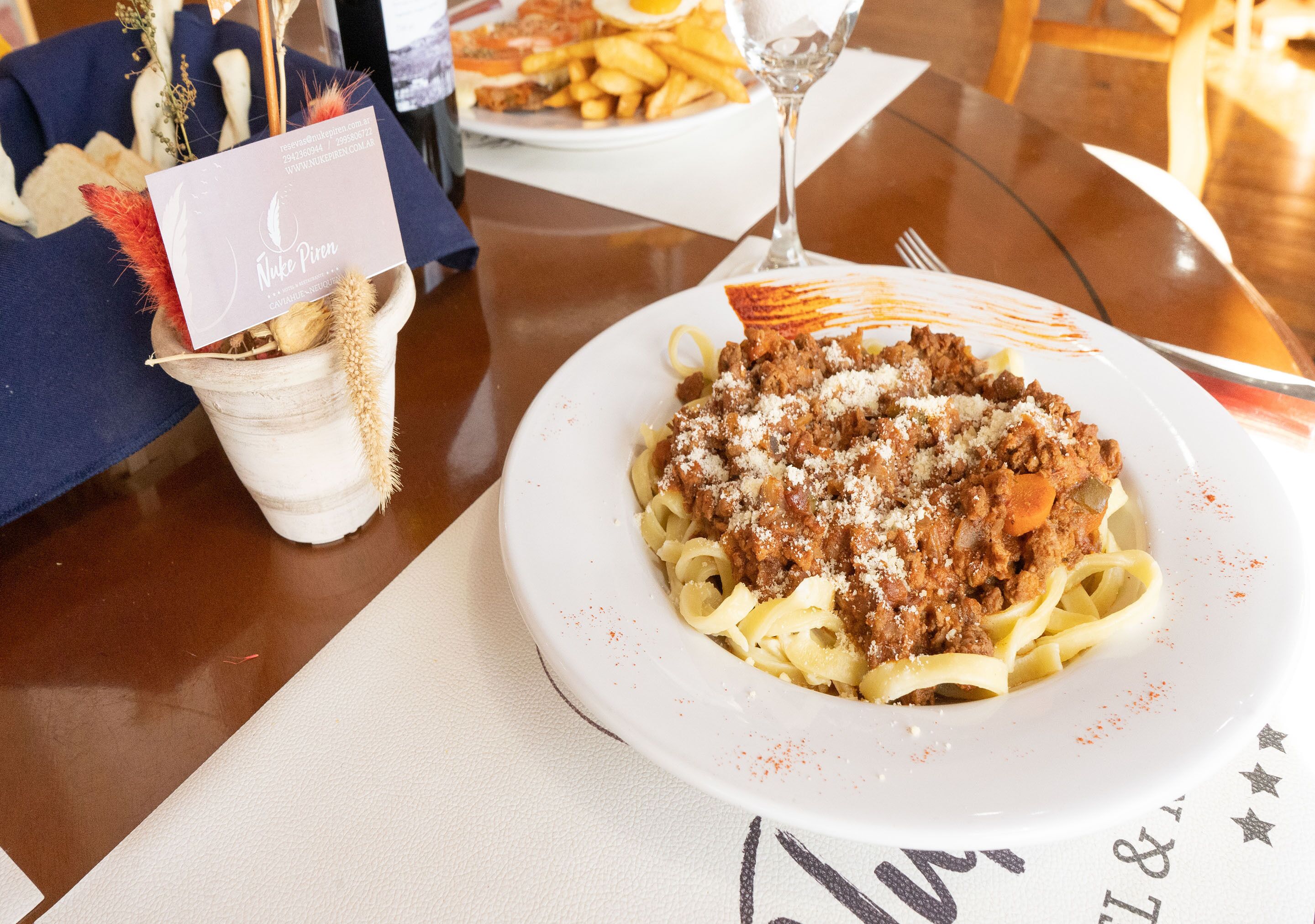 A dining table with a plate of pasta, a glass of water, and a menu.