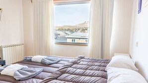 Habitación de hotel con dos camas, una ventana con vistas a edificios y colinas, y un radiador en la pared.