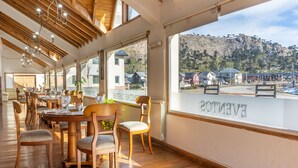 Un restaurante con mobiliario de madera y ventanas amplias que ofrecen vista a un paisaje montañoso.