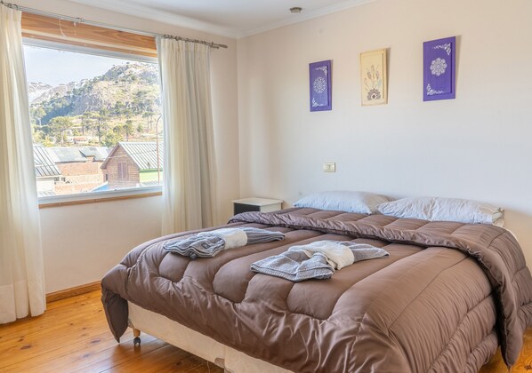Un dormitorio con una cama grande, una mesita de noche y un ventanal con cortinas.